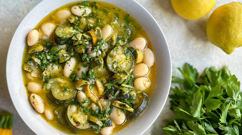 Butter beans with creamy courgette and green olive salsa plate with some lemons and herbs on the side