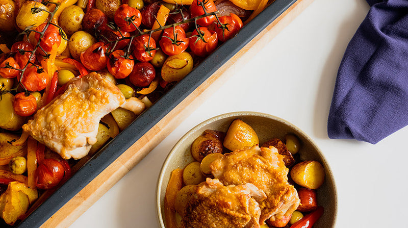 Chicken, chorizo and potatoes tray bake served in a bowl next to a naby blue napkin