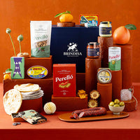 A styled gift assortment of Spanish food products, arranged on terracotta-coloured pedestals, set against a warm terracotta background.