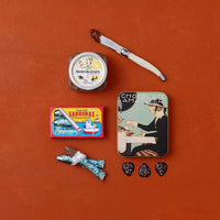 A styled flat-lay of Spanish food products: a jar of membrillo, a tin of chocolate leaves and a box of chocolate sardines.