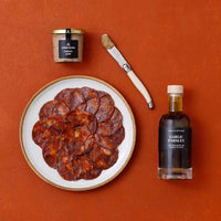 An overhead flat-lay of Spanish foods, including sliced chorizo on a plate, a jar of pate, and a bottle of flavoured olive oil.