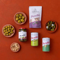 An overhead flat-lay of Perello brand food products arranged on a terracotta background, including almonds, oives and gherkins.