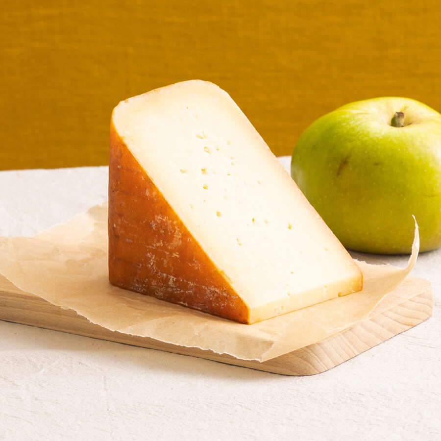 Wedge of mahon cheese on a wooden board with an apple in the background