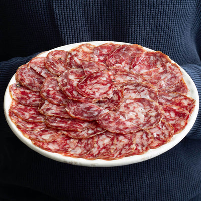 a man holding a plate of salchichon iberico, acorn fed. vibrant pink and marmolean