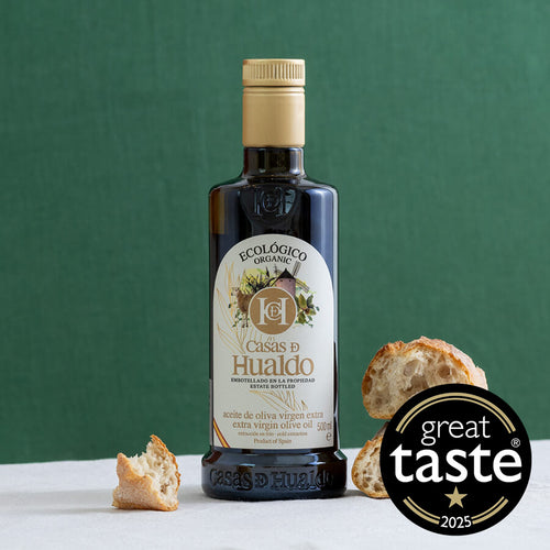 Bottle of Casa de Huado olive oil with bread slices on a green background, featuring the Great Taste 2025 award.