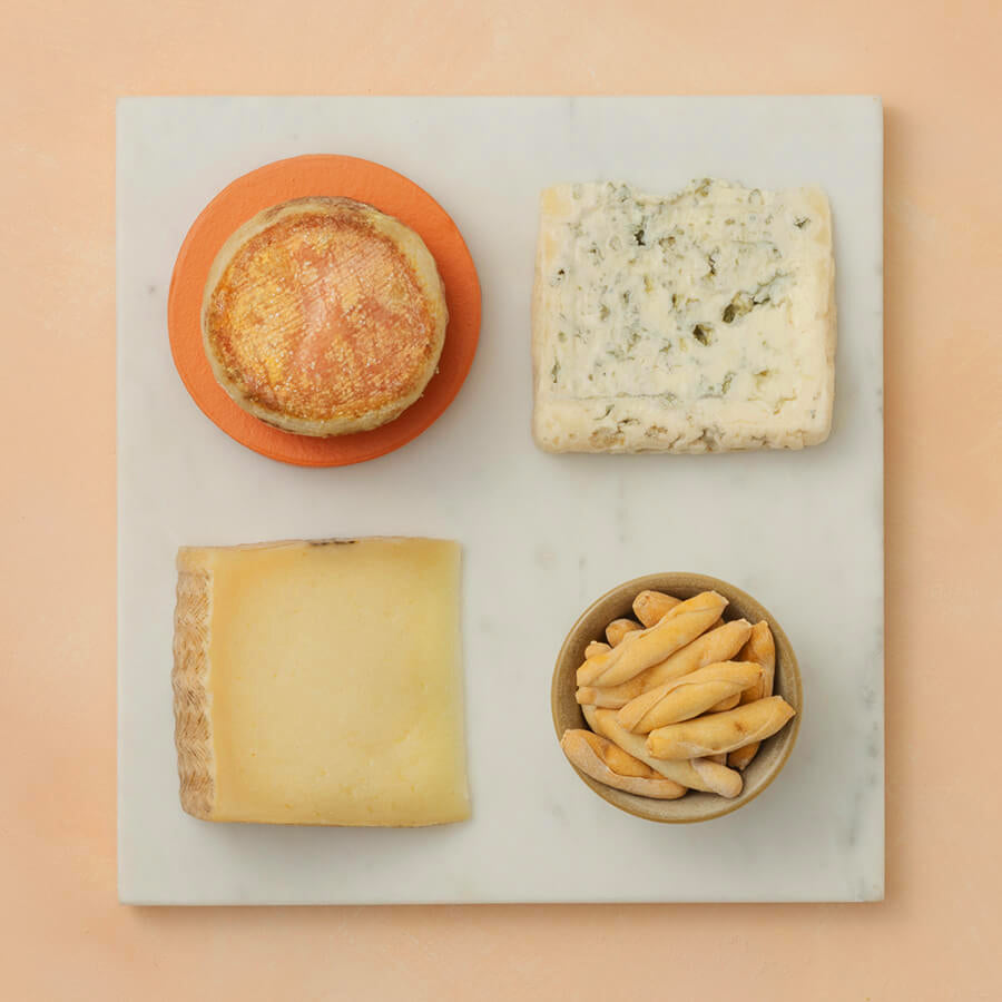 Assorted cheeses and bread on a marble board with a pink background
