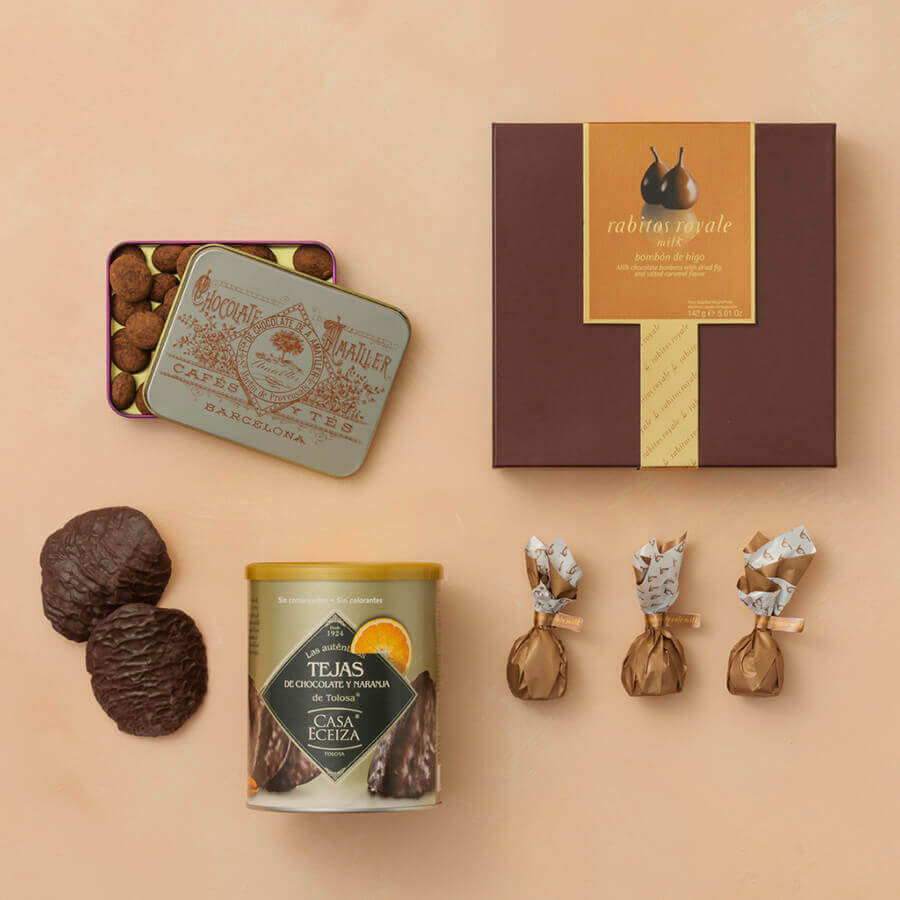Collection of chocolate products including a box, tin, and wrapped items on a beige background