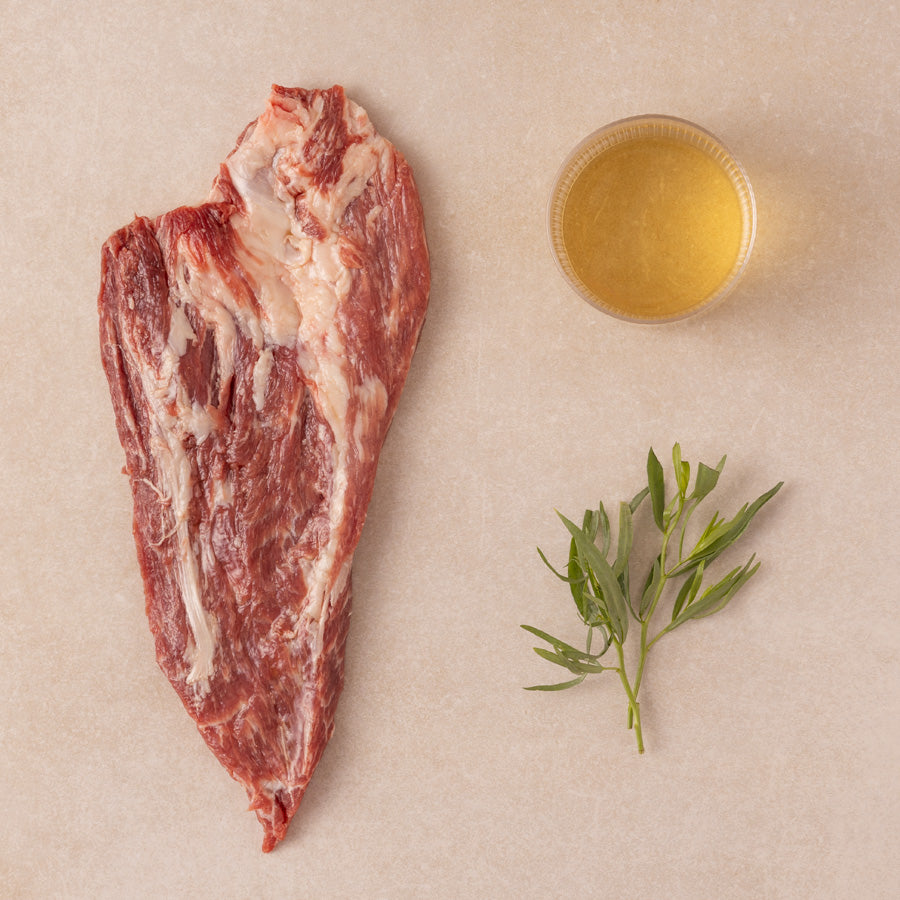 Raw meat with a small bowl of white wine and herbs on a beige background