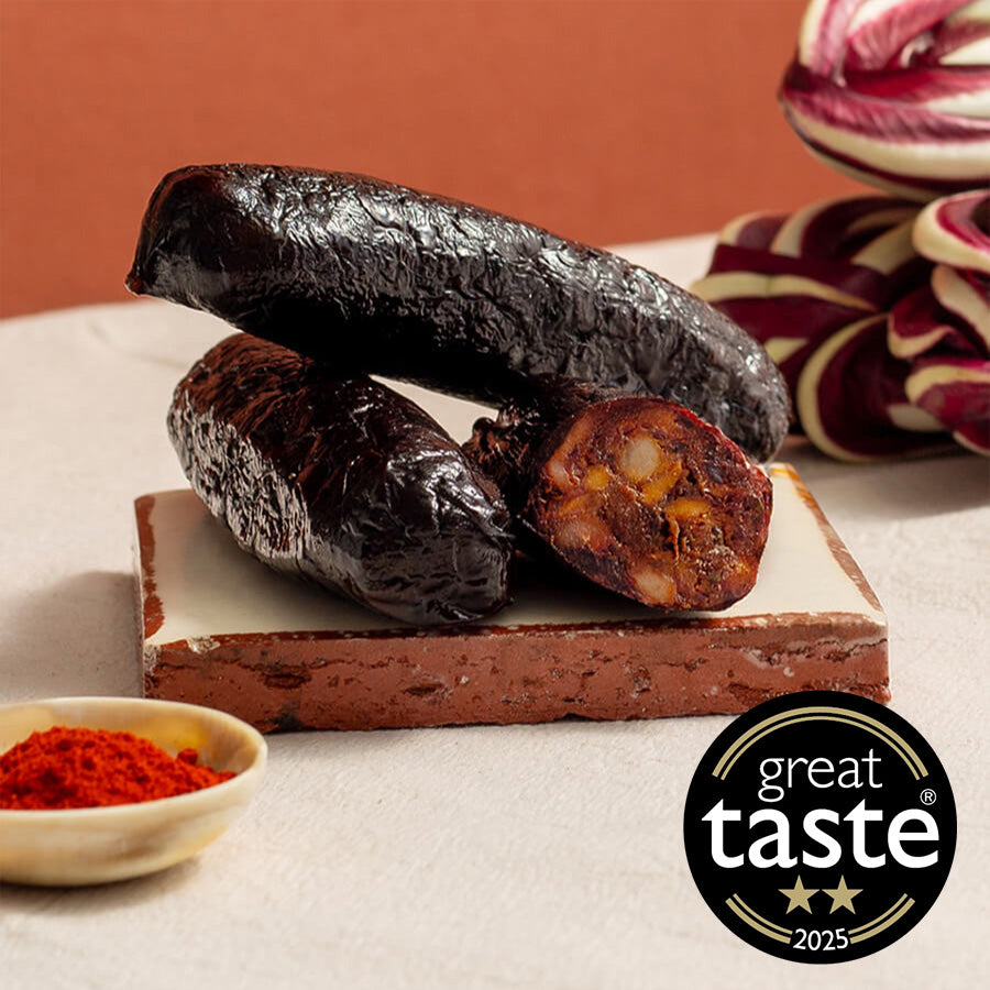Smoked black pudding on a cutting board with a 'Great Taste' award logo in the corner and paprika in the other