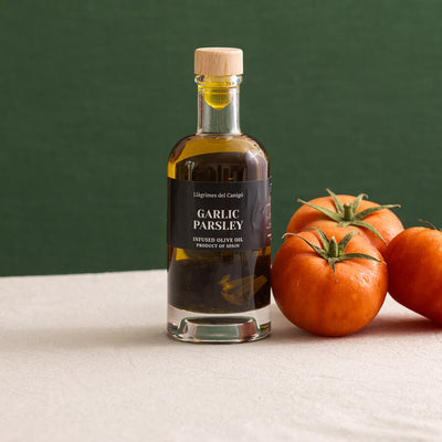 Bottle of garlic and parsley infused olive oil with tomatoes on a green background