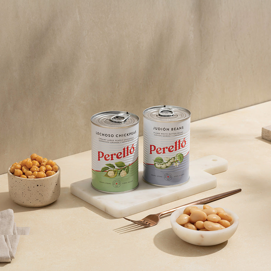 Two cans of Perello beans on a beige surface with bowls of beans and a fork.