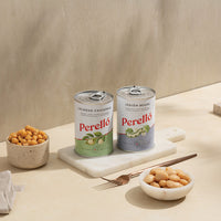 Two cans of Perello beans on a beige surface with bowls of beans and a fork.