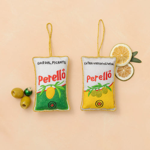 Two Perello olive oil packaging ornaments on a beige background with olives and lemon slices.