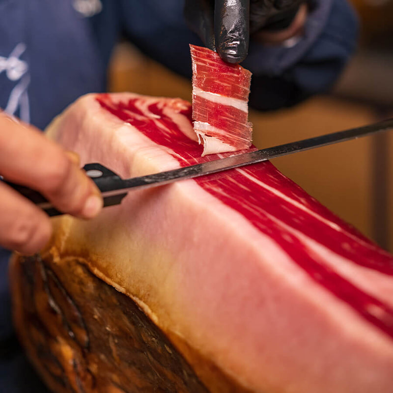 Person cutting a block of cured meat with a knife