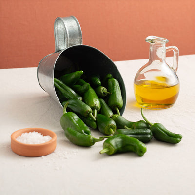 Pimientos de Padron falling off a scoop, a jar of extra virgen olive oil and sea salt flakes