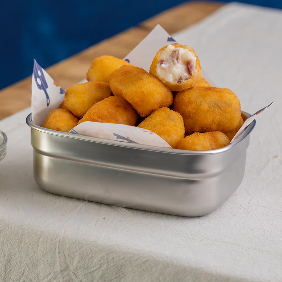 Metal container filled with golden brown fried ham croquetas
