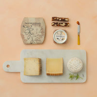Assorted cheeses on a marble board with quince, dried food and knife on a beige background