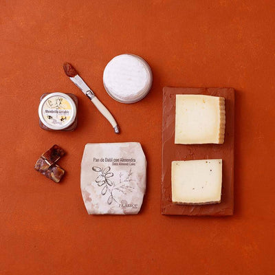 An overhead flat-lay of artisanal Spanish cheeses and membrillo on a terracotta background.