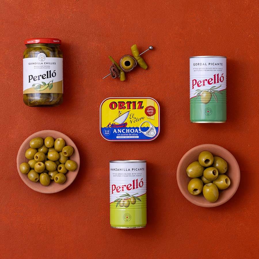 A styled flat-lay of Perelló products on a terracotta background and Ortiz anchovies.