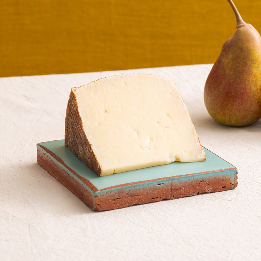 Arcano cheese wedge on a decorative tile with a pear in the background.