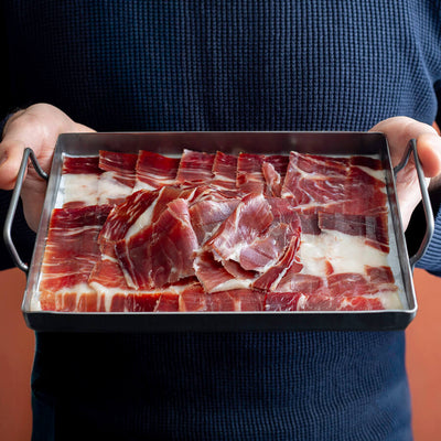 100% Iberico hand carved Ham slices in a tray hold by a man
