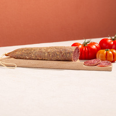 cured salchichon sausage in a chopping board with two slices and three tomatoes