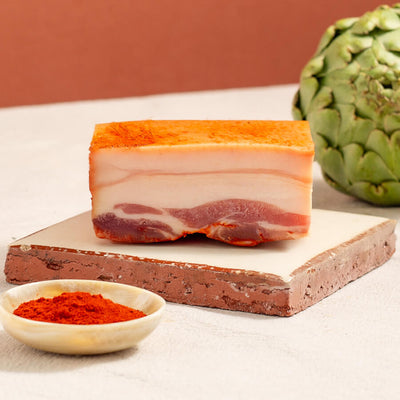 panceta with paprika piece on a tile, a bowl with paprika and artichokes