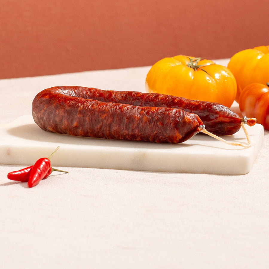 cured chorizo hoop in a marble board with two chillies and three yellow tomatoes