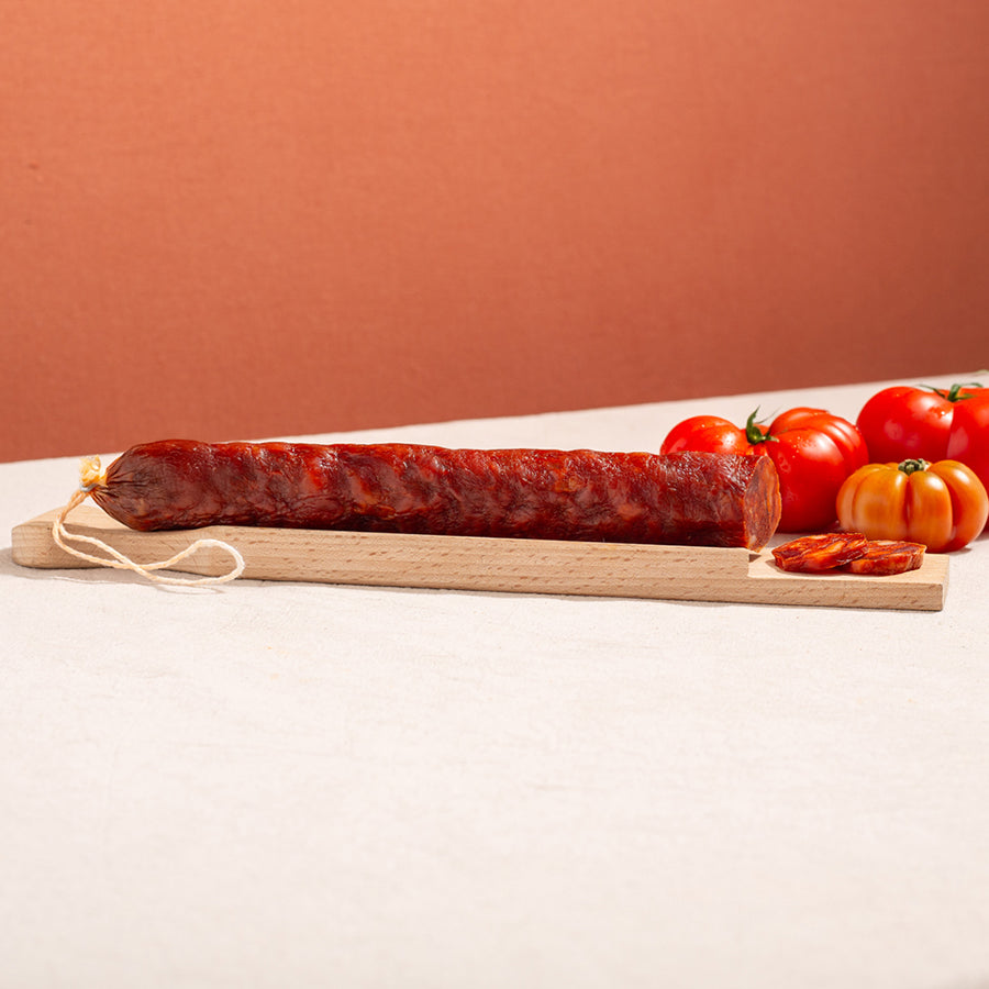 cured chorizo sausage in a chopping board with two slices and three tomatoes