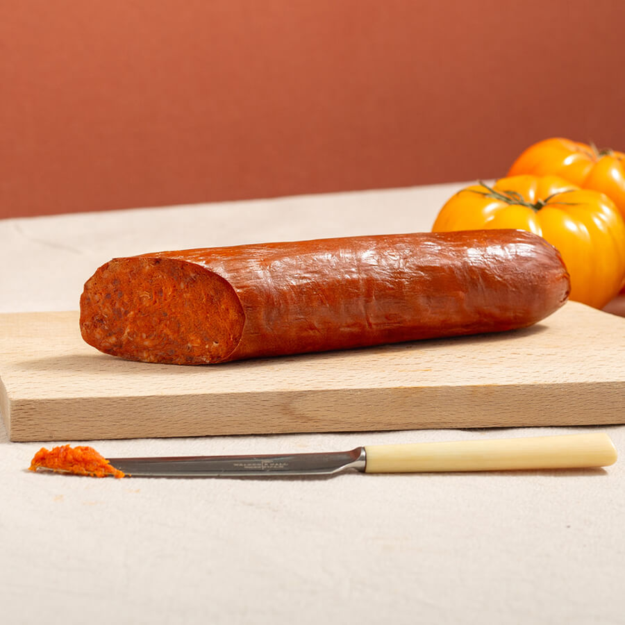 sobrasada, spreadable spanish sausage on a wood board. There's two yellow tomatoes at the back and one knife at the front with a bit of the sausage paste