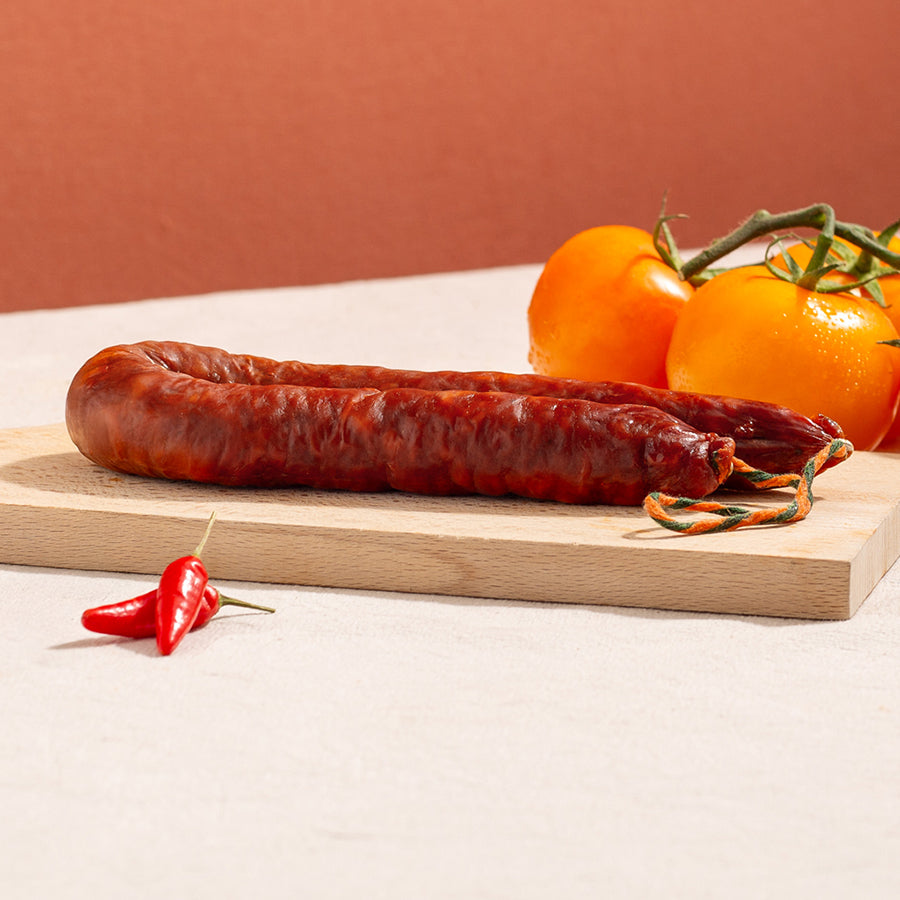 cured chorizo hoop in a chopping board with two chillies and three yellow tomatoes