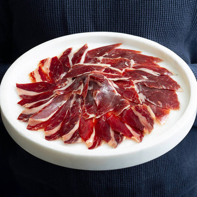 a man holding a large plate with hand carved iberico ham, acorn fed.