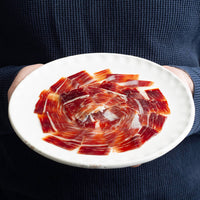 a man holding a plate with hand carved iberico ham, acorn fed.