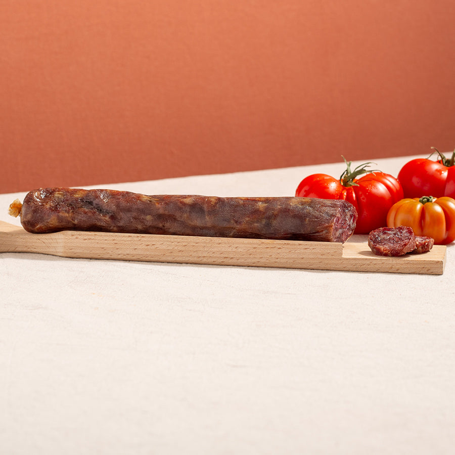 cured salchichon sausage in a chopping board with two slices and three tomatoes