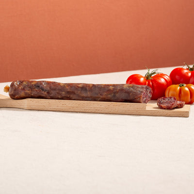 cured salchichon sausage in a chopping board with two slices and three tomatoes