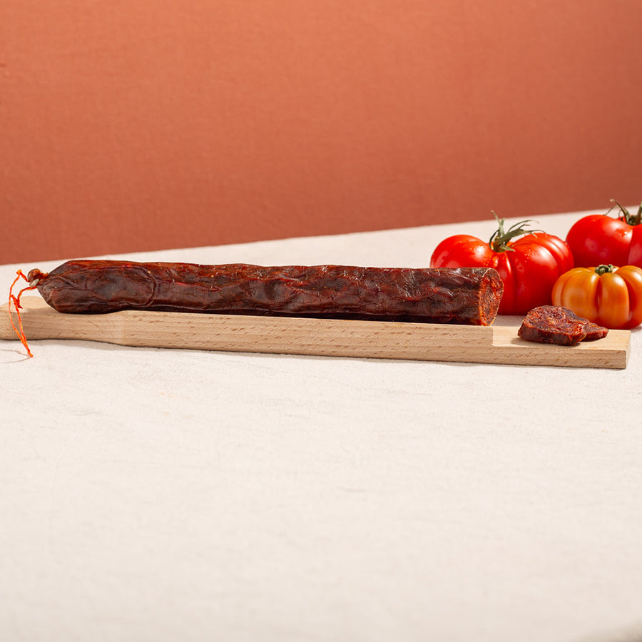 cured chorizo sausage in a chopping board with two slices and three tomatoes