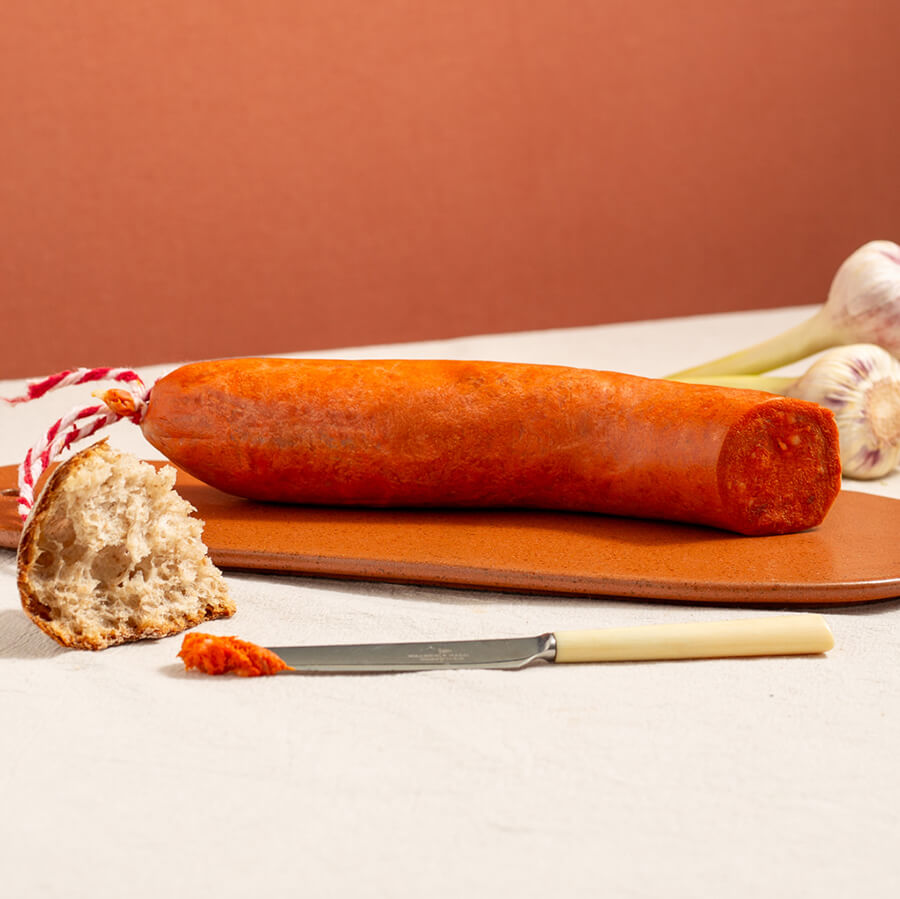 sobrasada from mallorca, spreadable Spanish sausage on a wood board. There's garlic at the back and, a bit of bread and one knife at the front with a bit of the sausage paste