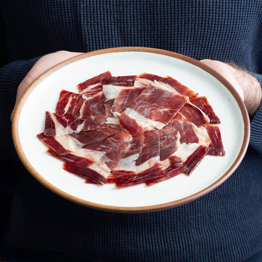 a man holding a plate with hand carved iberico ham, acorn fed.
