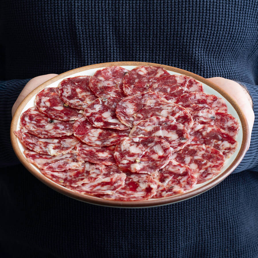 a man holding a plate of salchichon iberico, acorn fed. vibrant pink and marmolean