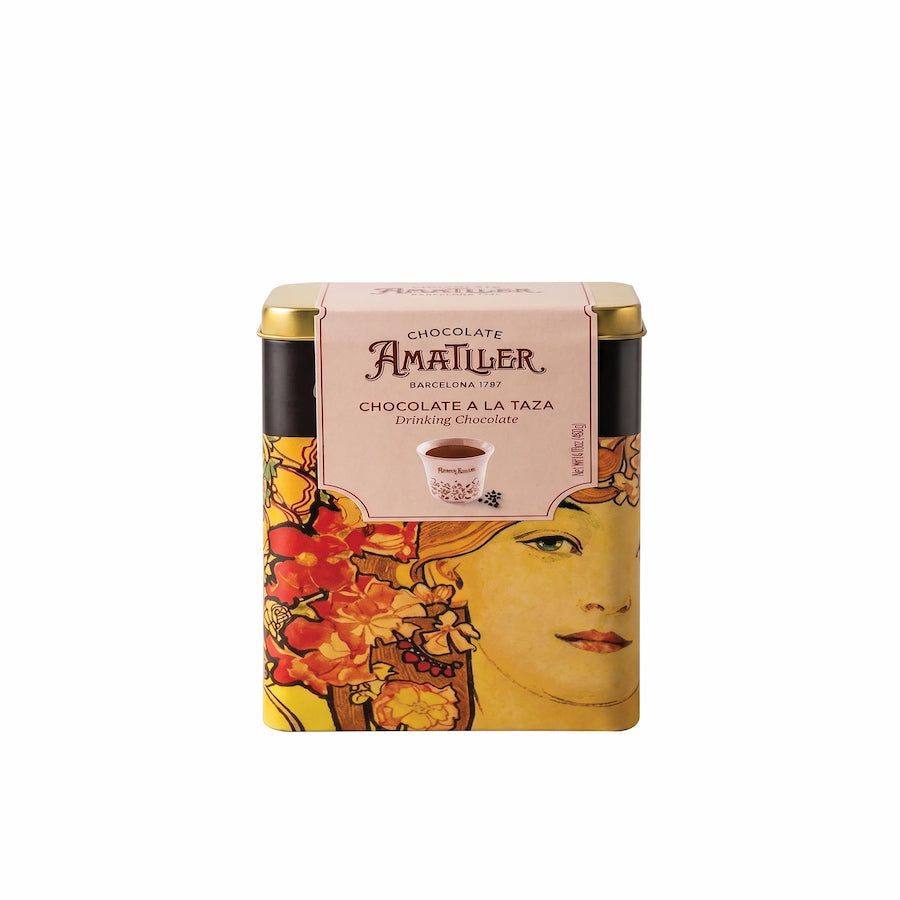 Amatller drinking chocolate tin, featuring a vintage Art Nouveau style illustration of a woman's face and red flowers, with a gold lid and a pink label.