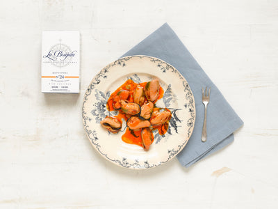 A plate with mussels in a tomato-based marinade on a white background.