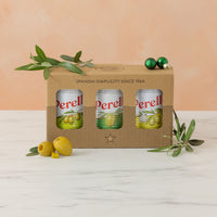 Perell olive oil packaging with three tins of olives on a white surface and peach-colored background