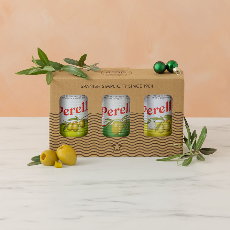 Perell olive oil packaging with three tins of olives on a white surface and peach-colored background