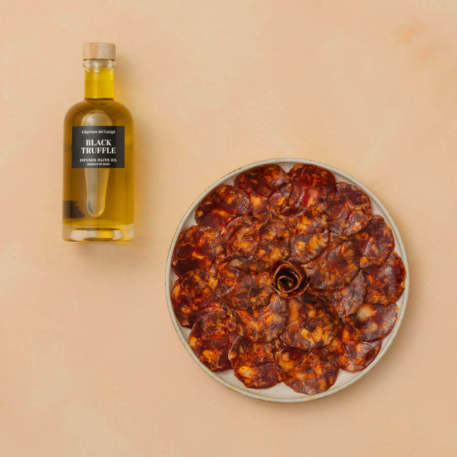 Dried cured meat on a plate with a bottle of truffle oil on a beige background