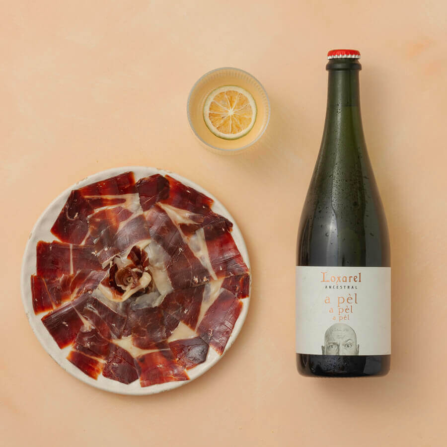Bowl of cured meat with a bottle of wine and glass on a beige background