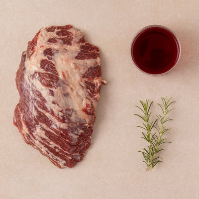 raw meat (ibesa presa), a glass of red wine and a sprig of thyme on a bage background 