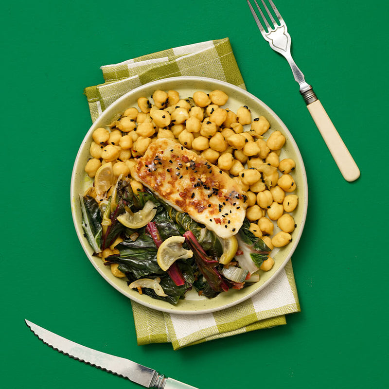 Plate of food with chickpeas, greens, and a piece of hallumi on a green background