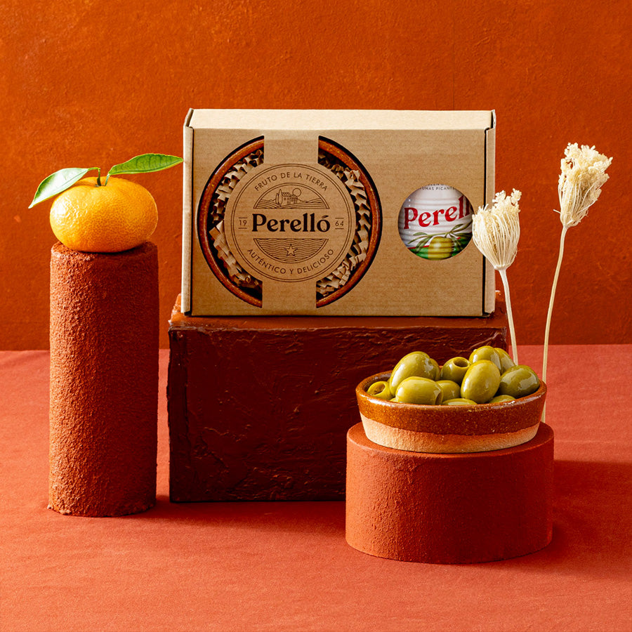 A Perello gift set made up of a tin of olives and a terracotta dish, displayed on a terracotta surface against a matching orange-brown background.