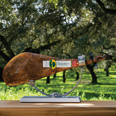 Senorio 100% iberico ham on th bone on a wooden board with a label in an outdoor setting