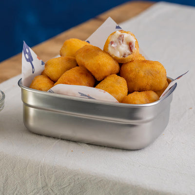 Metal container filled with golden brown fried ham croquetas 